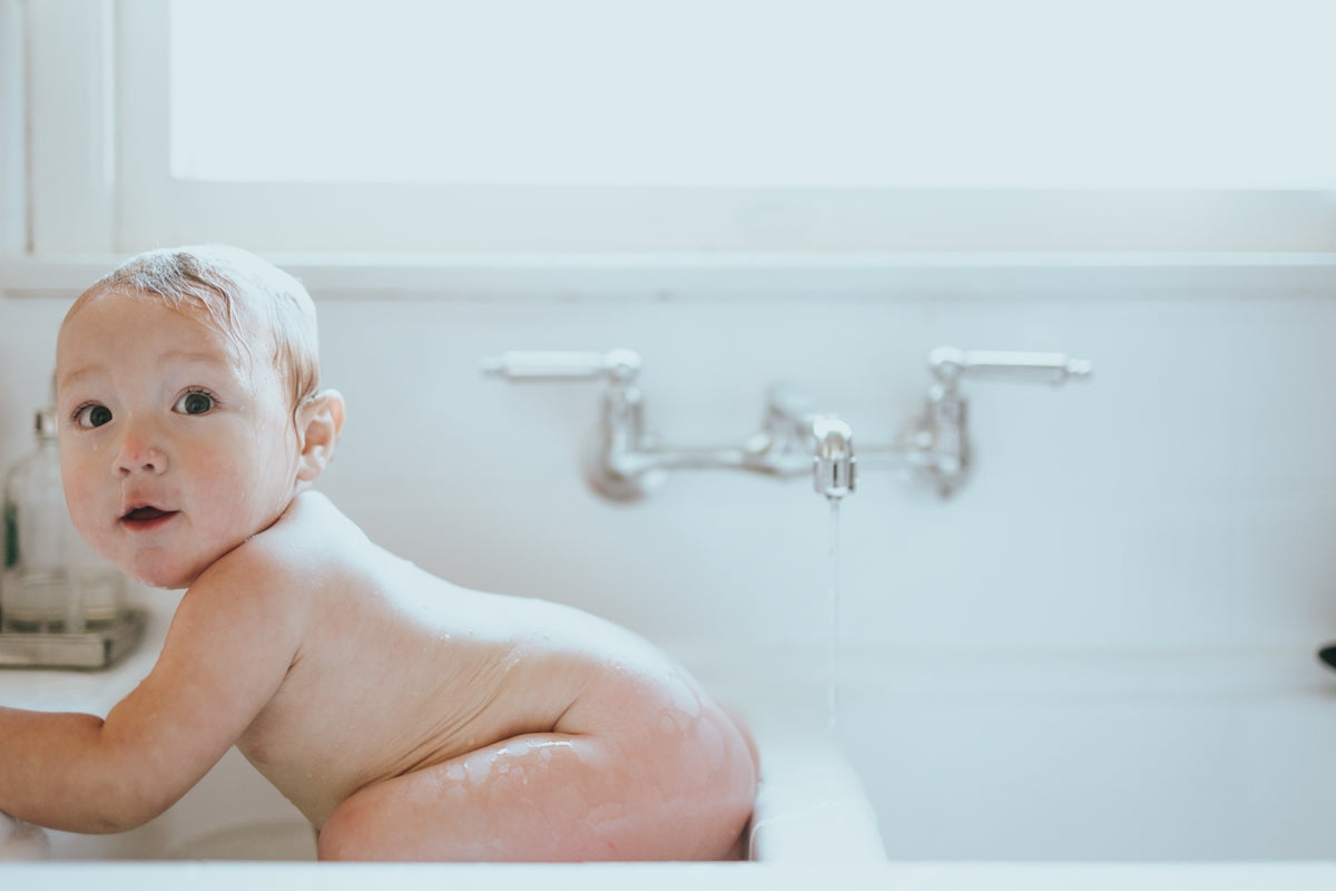 naked baby lying on white ceramic bathtub